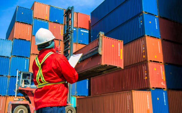 istock Man wears hardhat and reflection shirt and checking tablet with blurry metal containers in background. Concept of inventory and logistic management. 1480713307