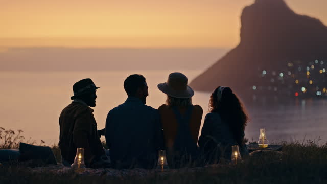 Nature, relax and friends watching a sunset while talking, chilling and bonding together on weekend trip. Conversation, silhouette and group of people speaking on mountain on a holiday or adventure.