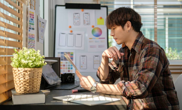 istock Side view of Asian male ux designer choosing color samples for mobile app while working in creative workplace. 1480715842