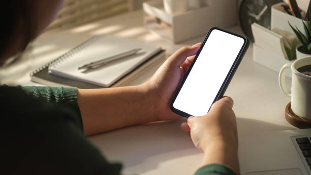 istock Over shoulder view of woman using mobile phone at working desk. Blank phone screen for create content and advertising. 1480715984