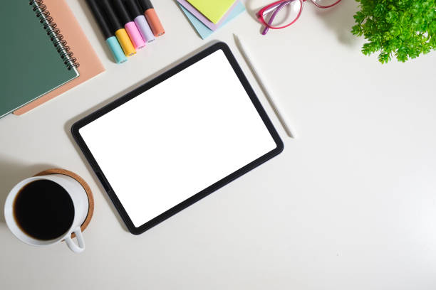 Digital tablet with blank screen, glasses, coffee cup and stationery on white table. Flat lay, top view with copy space.
