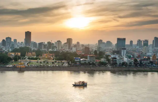Rooftop view,looking across to the Riverside area of Cambodia's capital city.Sunset over Royal Palace and high rise buildings as a small boat drifts by towards the Mekong river intersection.