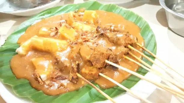 Photo of Sate Padang, popular beef skewer from Padang Indonesia, served on banana leaf, with special sauce and lontong