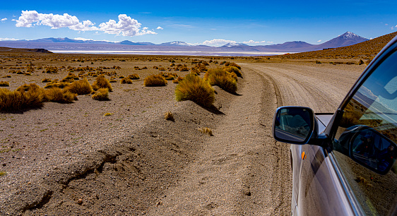 Car drives along rough road in Bolivian High Desert.  Mountains in background are actually hundreds of miles away.