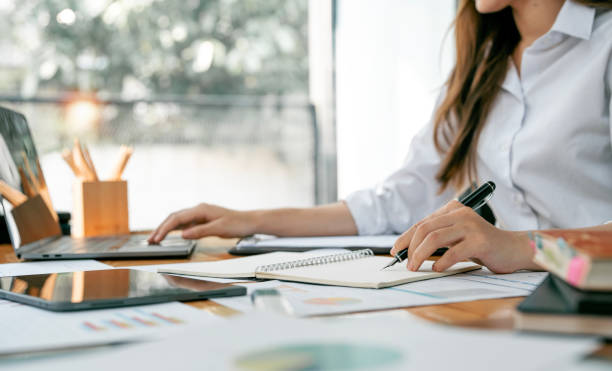 istock Cropped shot of businesswoman writing down note and using laptop computer while sitting at office. 1480724480
