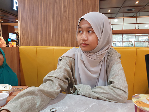 Samarinda, Indonesia. January 23th 2023. Asian muslim teenage girl sitting in cafe waiting for her meal