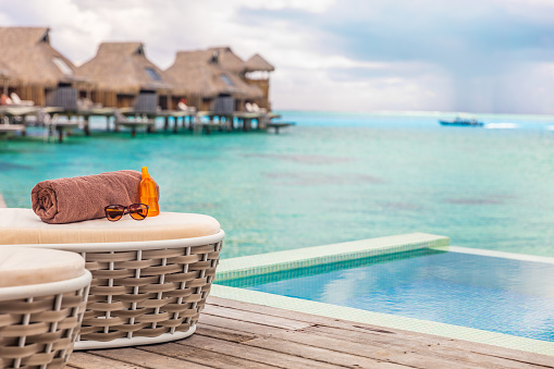Luxury Bora Bora overwater bungalow villas high end hotel in Tahiti, French Polynesia. Ocean view summer travel destination resort background, sun lounger with towel , sunscreen and sunglasses.