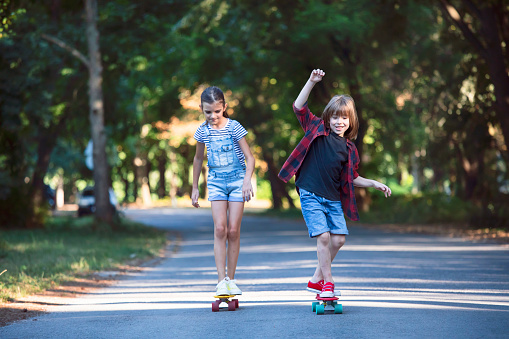 Two happy kids with skateboards walking in a park.