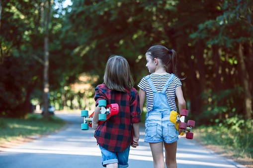 Two happy kids with skateboards walking in a park.