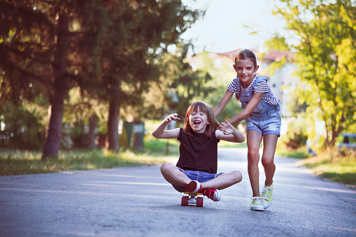 Two happy kids with skateboards walking in a park.