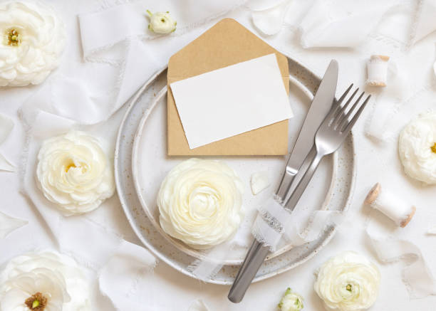 istock Wedding table setting with card and envelope near cream roses and white silk ribbons top view, mockup 1480738428