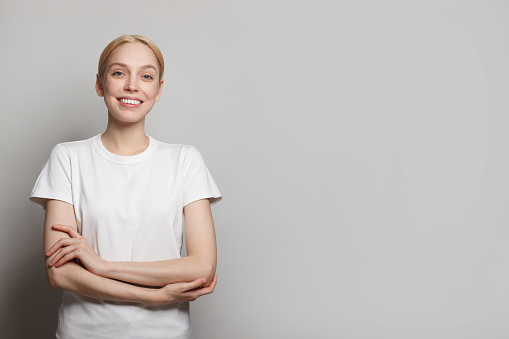 Cheerful young woman wearing white empty t-shirt smiling against white studio wall banner background