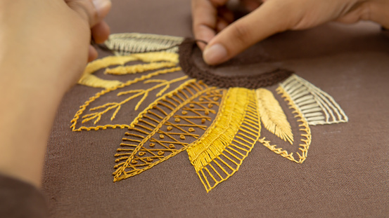 Close up of woman hands embroidering on brown tablecloth.