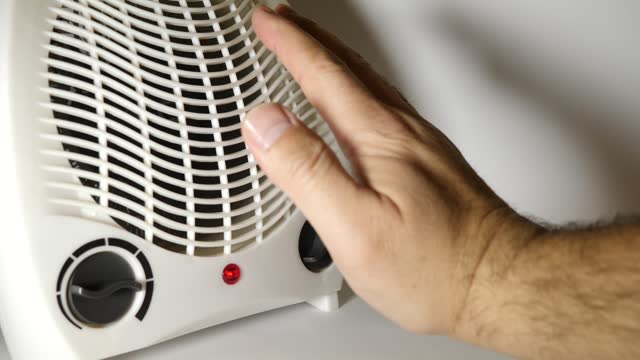 The person turns on the fan heater to heat the room. Portable, autonomous, electric space heating.