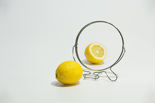 Half and one lemon reflected in the mirror on the white background.
