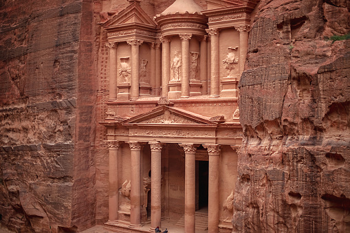 View of the Al-Khazneh Palace or Treasury in Petra, Jordan. The building is carved into a huge rock, has an elegant pediment and towering columns.