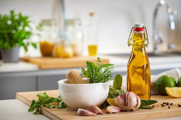 Close up view of a white mortar with fresh culinary herbs, a bottle of extra virgin olive oil and garlic shot on a cutting board placed on kitchen counter. High resolution 42Mp indoors digital capture taken with Sony A7rII and Sony FE 90mm f2.8 macro G OSS lens