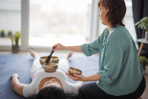 Masseuse performing Tibetan singing bowls massage on a client Young woman experiencing a Tibetan singing bowls massage at Shiatsu massage parlor mantra stock pictures, royalty-free photos & images
