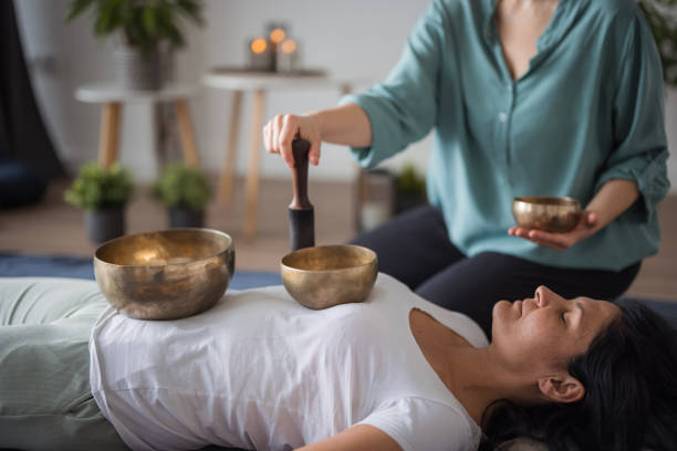 donna sdraiata sulla schiena durante la meditazione e il messaggio profondi delle campane tibetane - medicina alternativa foto e immagini stock