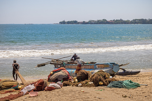 Galle, Sri Lanka - February 11th 2023:  People cleaning fishing nets on the beach outside Galle fish market as a part of the traditional fishing industry
