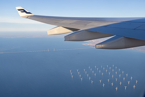 Copenhagen, Denmark - February 8th 2023:  Group of wind turbines and the Oresund Bridge which is connecting Denmark and Sweden seen under the wing of an Airbus 330-300 from Finnair during take off from Copenhagen Airport