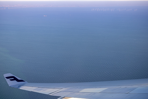 Copenhagen, Denmark - February 8th 2023:  Group of wind turbines and the Oresund Bridge which is connecting Denmark and Sweden seen over the wing of an Airbus 330-300 from Finnair during take off from Copenhagen Airport