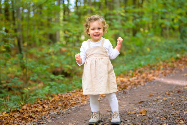 Full length shot of a little smiling girl curiously looking in the forest in autumn
