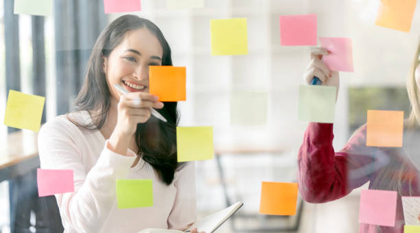 istock Young businesswoman creative team using post it notes in glass wall to writing strategy business plan to development grow to success. 1480783378
