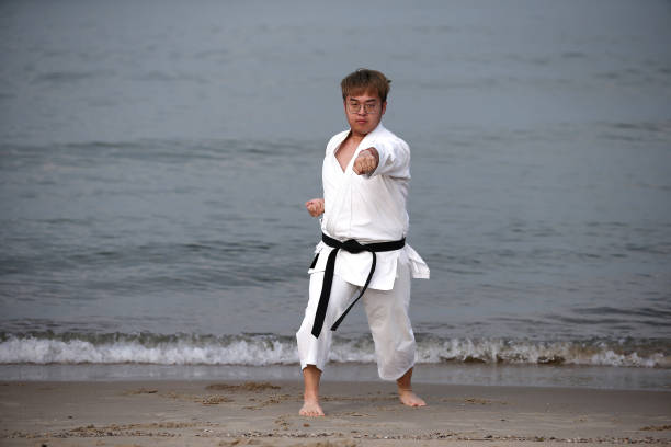 An Asian man is practicing taekwondo by the beach.