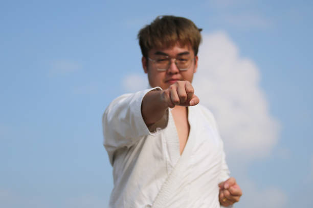 An Asian man is practicing taekwondo by the beach.