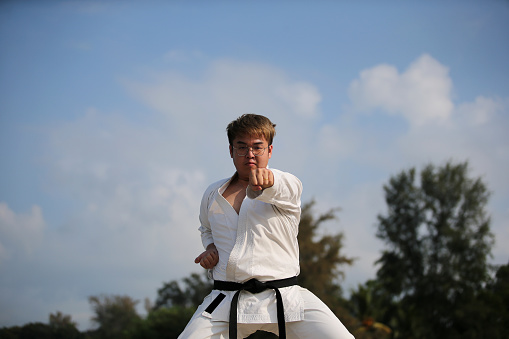 An Asian man is practicing taekwondo by the beach.