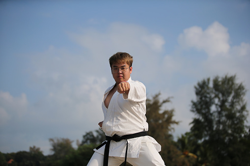 An Asian man is practicing taekwondo by the beach.
