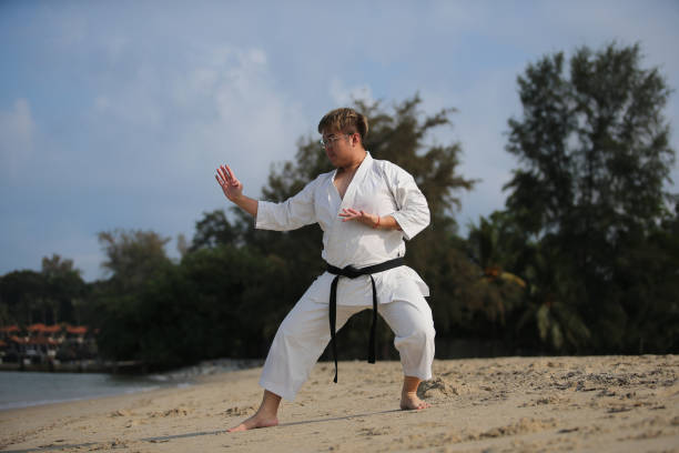 An Asian man is practicing taekwondo by the beach.