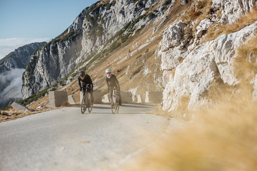 A photo captures a small group of road cyclists training in the beautiful mountainous terrain, dressed in their cycling gear, helmets, and gloves. The focus is on their determination as they prepare for a triathlon.
