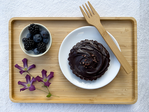 Vegan and gluten free chocolate tart served with organically homegrown berries, served with sustainable bamboo fork on bamboo tray.