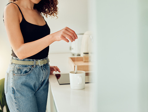 Woman hand holding tea bag over cup of boiling water, making chai in kitchen taking a break. Female barista woman working at cafe or coffee shop counter, hot drink during office lunch break.