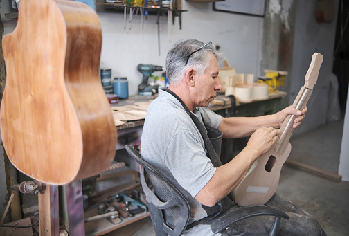 middle-aged latino man sanding a ukulele in the middle of his carpentry shop