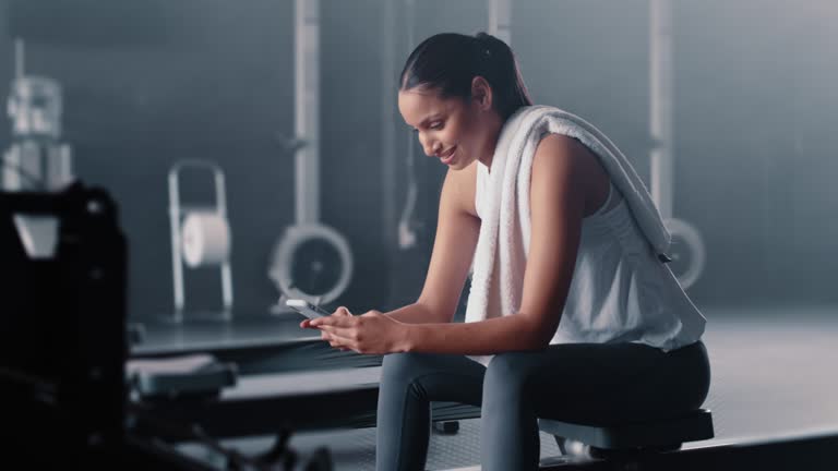 Smartphone, woman and rest in gym, smile and social media of workout, health progress or texting app. Happy female, sports break and mobile technology of fitness, training or digital exercise network