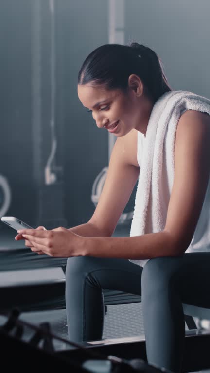 Smartphone, woman and smile in gym on break for social media, reading chat message and texting app. Happy female, fitness and rest on mobile technology of sports, training or digital exercise network