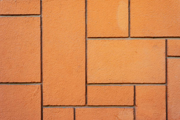 Closeup of a beige wall featuring a textured surface and square tile design, exuding a rustic and industrial vibe. Perfect as a neutral background or architectural detail for various projects.