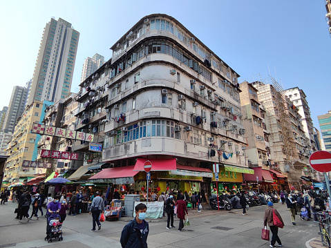 People walking at a busy intersection by an old fashioned Tong Lau apartment building in Sham Shui Po district, Kowloon, Hong Kong.