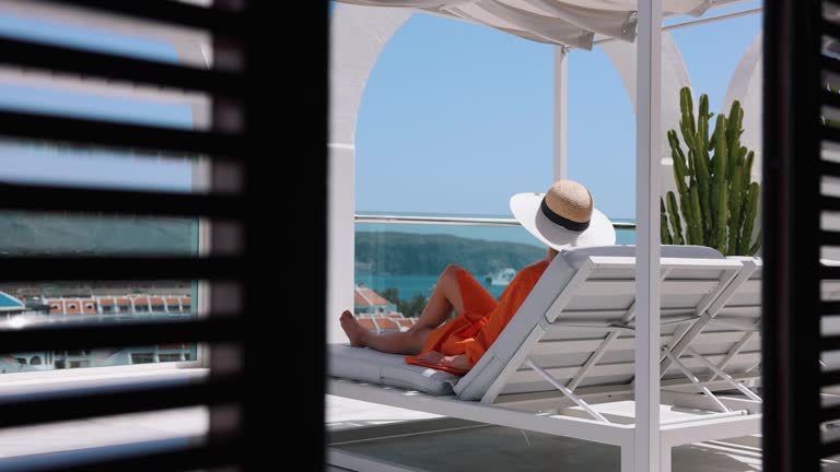 woman relaxing in sunbed and enjoy the summer vacation at luxury rooftop penthouse terrace with sea view. rear view