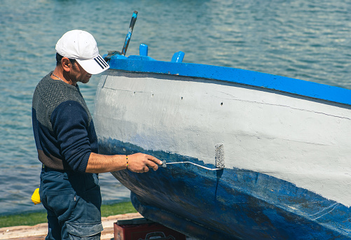 Bari, Puglia, Italy - April 8 2023: Fisherman repairing and painting an old wooden fishing boat at the port quay in Bari, Puglia Italy