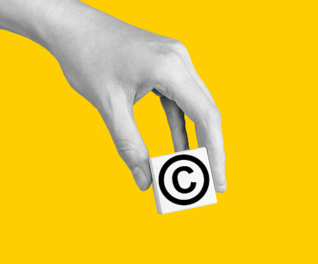 World copyright day. Hand with intellectual property protection, patent law sign in circle on cube. High quality photo