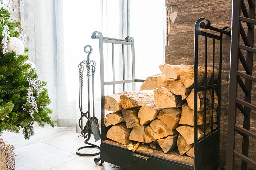 Stack of firewood logs by a fireplace and Christmas tree in hotel lobby. Christmas post card.