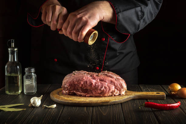 le chef prépare de la viande de veau crue. avant la cuisson, le chef ajoute du poivre au bœuf. un plat national est en cours de préparation dans la cuisine - veal calf meat baking photos et images de collection