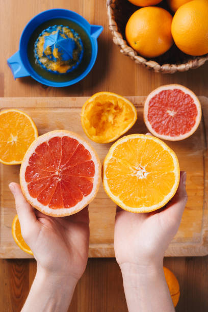istock Hands holding cut  orange and grapefruit above wooden cutting board, table top view 1480830985