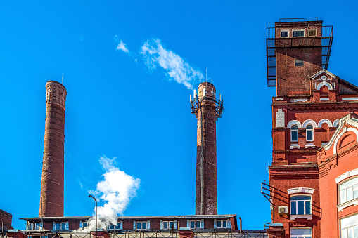 The red brick roofline of an old textile mill converted to modern offices in North Andover Massachusetts. Smoke stack and mill building details with brilliant blue sky background with room for copy.