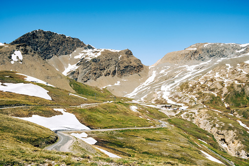 Col de l'Iseran, France - June 11, 2022: Near the highest point of a mountain pass through the French Alps, the road winds up through the barren Alpine mountain landscape. Remnants of snow melt away under the spring sun.