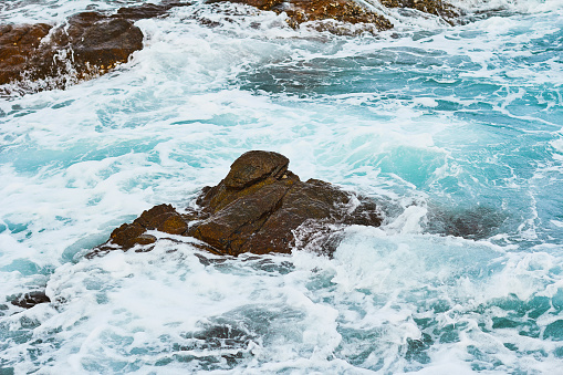 Pattern of sea surface and rocky shore. Coast island with blue turquoise water beats on rocky reef. Closeup seascape. Sea wave rock crush. Sea turquoise water and sea foam